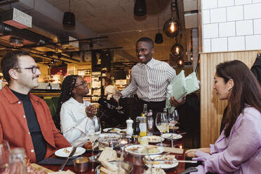 Glücklicher Mann im Gespräch mit männlichen und weiblichen Freunden während einer Dinnerparty im Restaurant - MASF28367