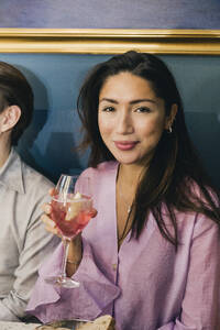 Porträt einer lächelnden Frau mit Wein, die neben einem männlichen Freund in einer Bar sitzt - MASF28382