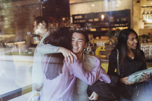 Man embracing female friend seen through glass of restaurant - MASF28383