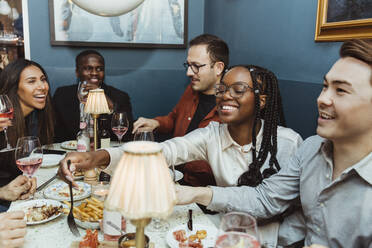 Multirassische weibliche und männliche Freunde beim Essen am Tisch im Restaurant - MASF28385