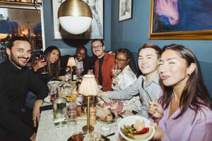 Porträt eines lächelnden gemischtrassigen männlichen und weiblichen Freundes während einer Dinnerparty in einer Bar - MASF28387