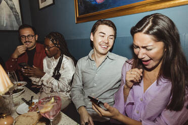 Happy women using smart phone while sitting by male friends at restaurant during party - MASF28388