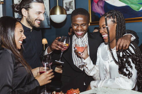Fröhliche weibliche und männliche Freunde mit Weingläsern beim Feiern in einer Bar - MASF28393