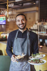 Porträt eines lächelnden männlichen Kellners mit Essen im Restaurant - MASF28403