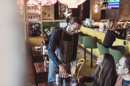 Smiling waiter pouring wine to male and female customers in bar - MASF28409