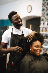 Smiling male barber cutting hair of female customer in salon - MASF28444