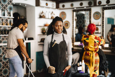 Portrait of confident young female hairdresser with hands in pockets at barber shop - MASF28465