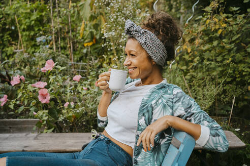 Smiling female farmer drinking coffee while sitting at urban farm - MASF28548