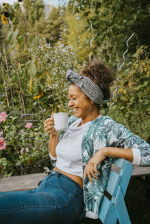 Female environmentalist with coffee cup laughing in community garden - MASF28549