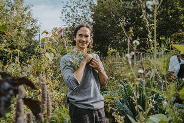 Portrait of smiling male agricultural shareholder with plant in urban garden - MASF28570