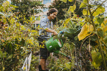 Smiling male volunteer watering plants in farm - MASF28580