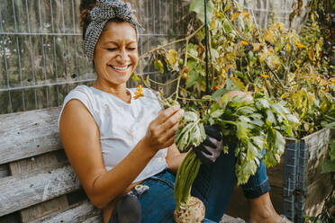 Happy female environmentalist with vegetable sitting in urban farm - MASF28605