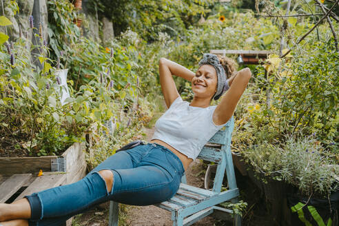 Smiling female farmer with hands behind head resting in urban garden - MASF28608