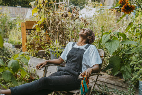 Happy female agricultural shareholder relaxing on chair in urban garden - MASF28614