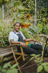 Portrait of female environmentalist sitting on chair in community garden - MASF28616