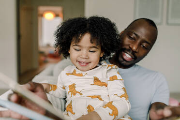 Happy daughter reading book with father at home - MASF28637