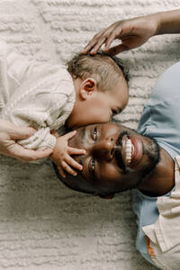 Männliches Kleinkind küsst Vater auf Decke liegend zu Hause - MASF28658