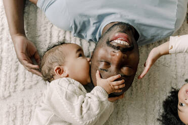 Baby boy kissing father lying on blanket at home - MASF28659