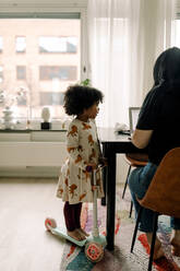 Daughter looking at mother freelancing on laptop in living room - MASF28667