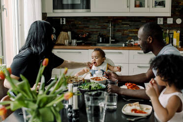 Mother feeding son sitting with family in kitchen - MASF28685