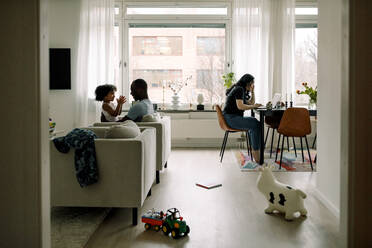 Father talking with daughter while mother working on laptop at home - MASF28691