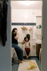 Mutter und Tochter beim gemeinsamen Zähneputzen im Badezimmer zu Hause - MASF28707