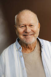 Porträt eines lächelnden älteren Mannes vor braunem Hintergrund - MASF28736