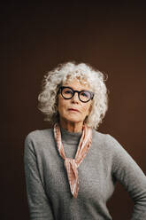 Portrait of elderly woman wearing eyeglasses over brown background - MASF28739