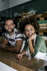 Smiling female owner with hand on chin by male colleague in bakery - MASF28780