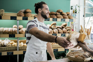 Lächelnder männlicher Besitzer gibt einem Kunden in einer Bäckerei ein Brot - MASF28785