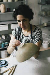 Craftswoman painting bowl at ceramics store - MASF28817