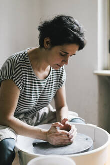 Mature female potter modeling clay in workshop - MASF28833