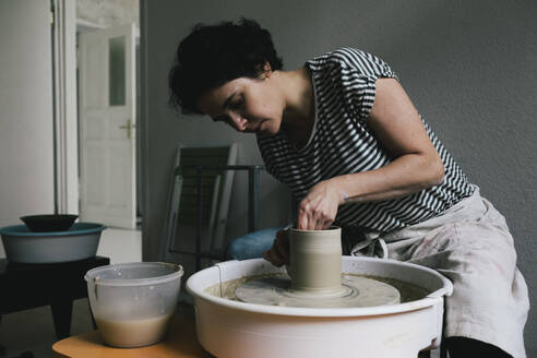 Female potter modeling shape to pot at ceramics workshop - MASF28836