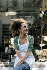 Lächelnde Unternehmerin schaut weg, während sie vor einer Bäckerei sitzt - MASF28878