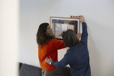 Heterosexual couple measuring level for hanging picture frame on wall while relocating in new house - MASF28892