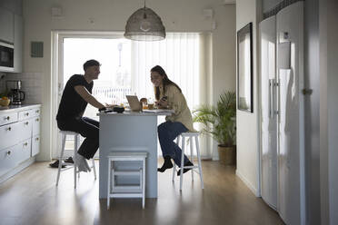 Lächelndes junges Paar benutzt Laptop bei der Arbeit in der Küche - MASF28907