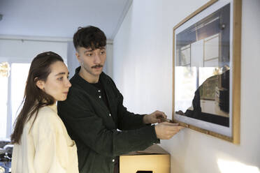 Young man measuring picture frame standing by girlfriend at home - MASF28925