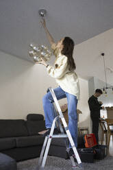 Woman installing chandelier while relocating in new house - MASF28938