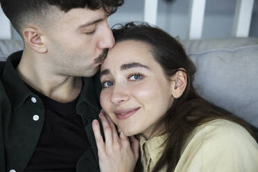 Young man kissing girlfriend's forehead in bedroom at home - MASF28948