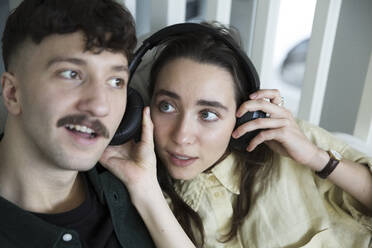 Heterosexual couple listening music through headphones at home - MASF28949