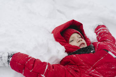 Boy wearing warm clothing lying on snow in winter - SEAF00519