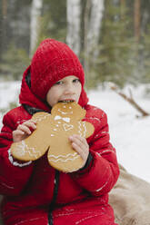 Junge isst Lebkuchenplätzchen sitzend im Winter - SEAF00521