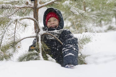 Glücklicher Junge, der sich an einem Tannenbaum im verschneiten Wald erfreut - SEAF00524