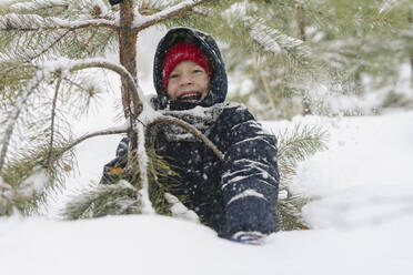 Happy boy enjoying by fir tree in snowy forest - SEAF00524