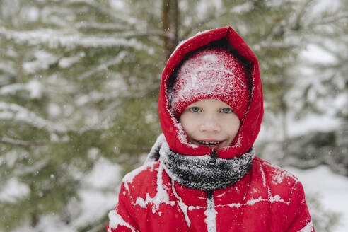 Glücklicher Junge mit Schnee auf Strickmütze und warmer Kleidung im Wald - SEAF00527