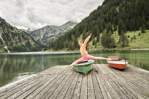 Cheerful girl jumping and doing splits in air over jetty - DIKF00627