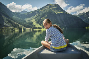 Smiling girl sitting in rowboat on lake - DIKF00629