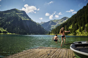 Sister and brother jumping into Vilsalpsee lake - DIKF00635