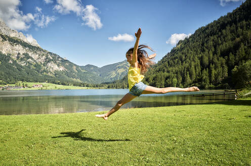 Girl jumping and doing splits in air at Haldensee lakeshore - DIKF00636
