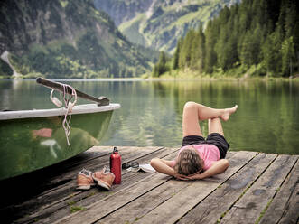 Relaxed woman lying down on jetty by lake - DIKF00643